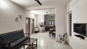 A living room with a sofa, coffee table, and TV. There is a kitchen area with a dining table and chairs. - Cheruthodath Serviced Apartments (Ernakulam)