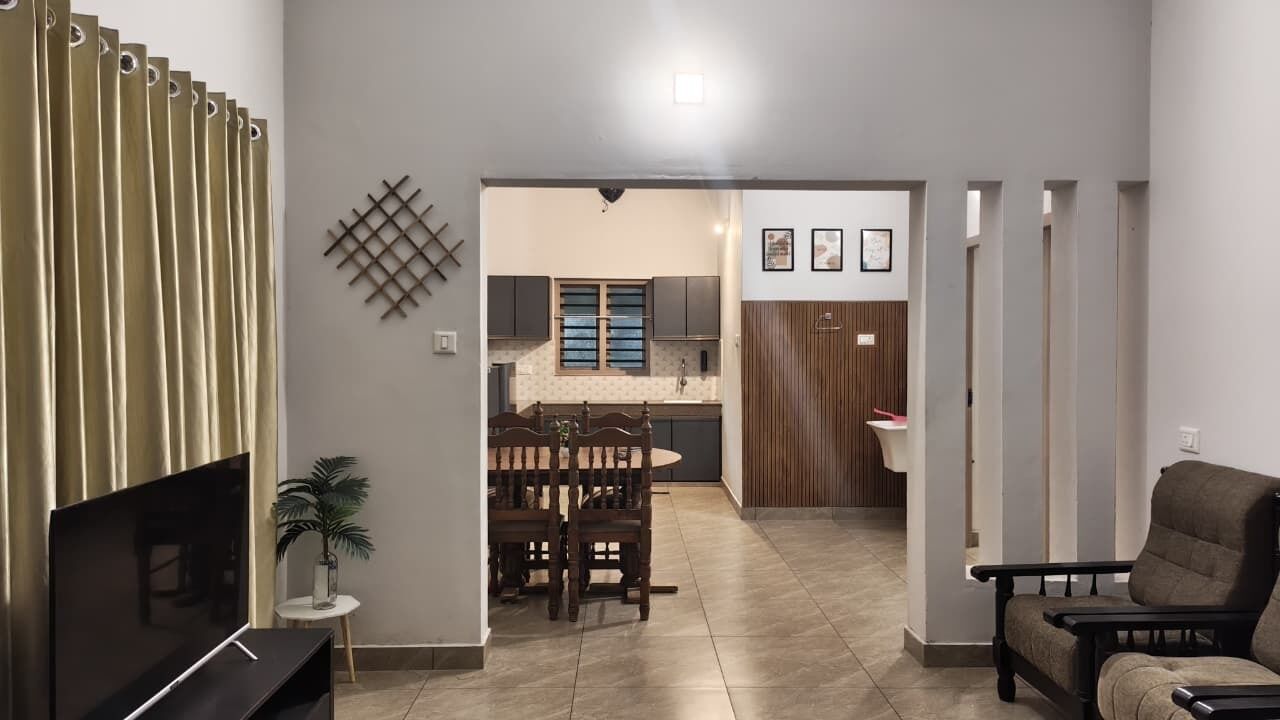 A living room with a TV, a dining area with a table and chairs, and a kitchen in the background.