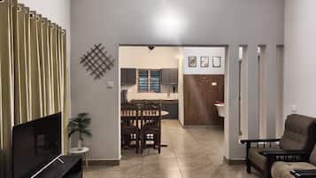 Una sala de estar con televisor, un comedor con mesa y sillas, y una cocina al fondo.
