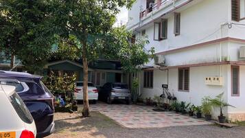 A residential building with a covered parking area, a tree, and several parked cars.
