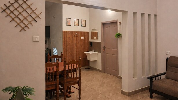 A dining area with a wooden table and chairs, a kitchen with a sink, and a door leading to another room.
