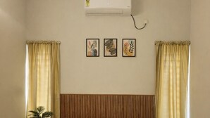 Un dormitorio con cama, cortinas, aire acondicionado y una mesita con una planta.