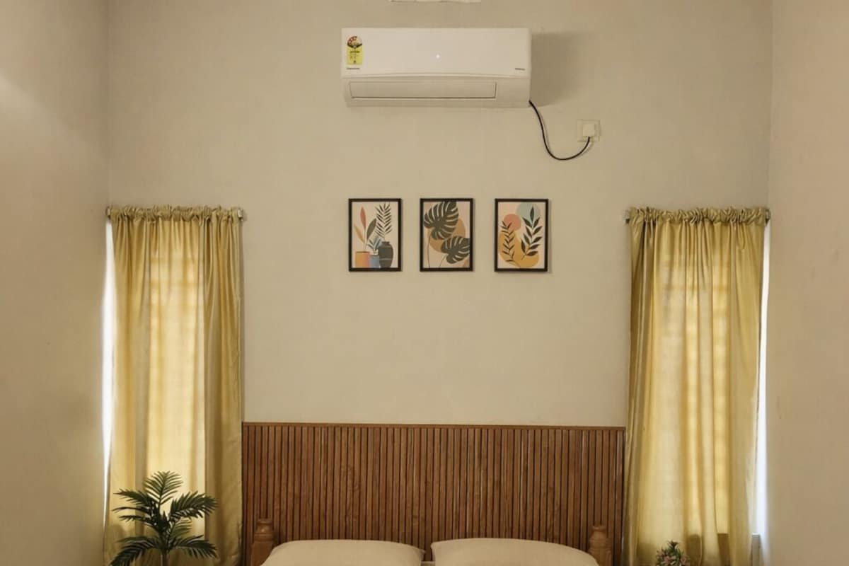 A bedroom with a bed, curtains, an air conditioner, and a small table with a plant.