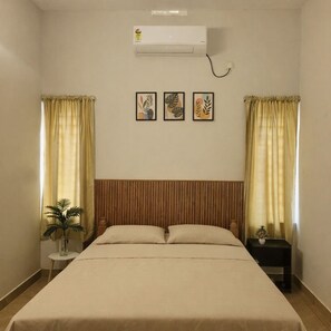 A bedroom with a bed, curtains, an air conditioner, and a small table with a plant. - Cheruthodath Serviced Apartments (Ernakulam)