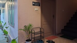 A hallway with a sign for 'A1 Cheruthodath Apartments', a potted plant, a shoe rack, and a door.