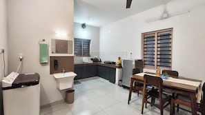 A compact kitchen with a sink, countertop, and a dining area with chairs and a table. - Cheruthodath Serviced Apartments (Ernakulam)