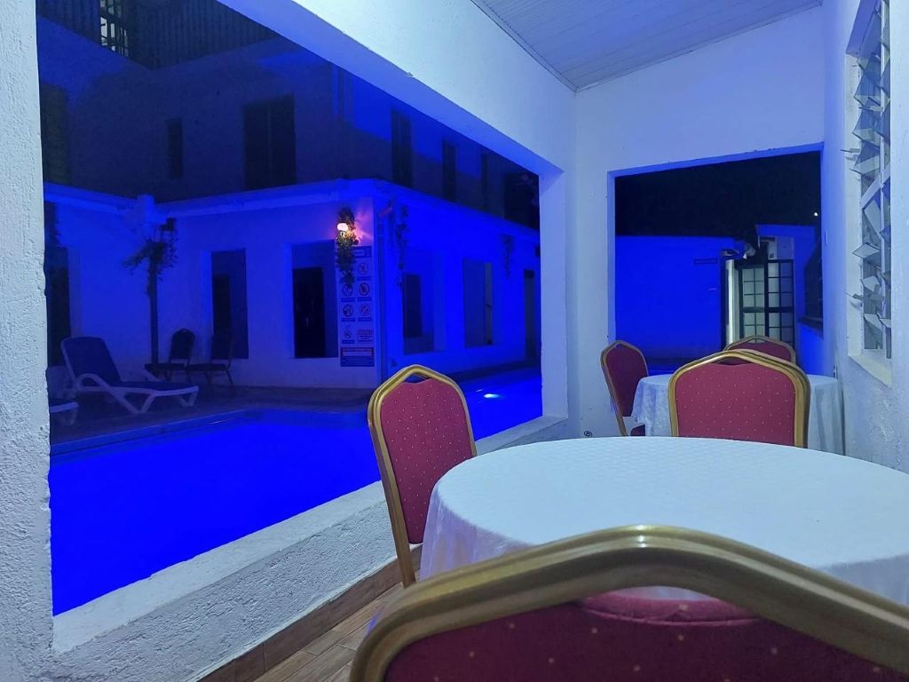 Uma área junto à piscina com mesa e cadeiras, piscina e um edifício com varandas.