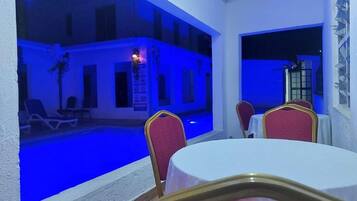 Uma área junto à piscina com mesa e cadeiras, piscina e um edifício com varandas.