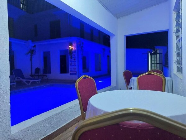 A poolside area with a dining table and chairs, a pool, and a building with balconies.