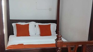 Een hemelbed met houten frame en witte beddengoed, een houten stoel met een bekleed zitoppervlak en een betegelde vloer.