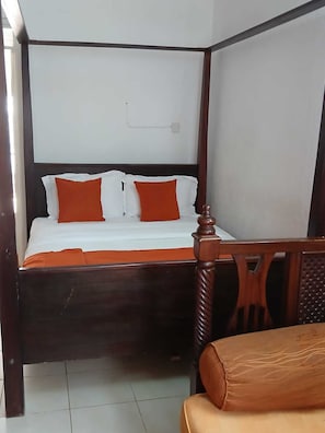 A four-poster bed with a wooden frame and white bedding, a wooden chair with a cushioned seat, and a tiled floor. - Executive Studio in Kisumu. Complimentary wifi, secure parking & quiet stay (Kisumu)