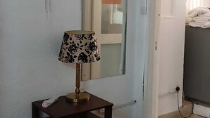 Een kamer met een bed, een nachtkastje met een lamp, een ventilator aan de muur en een spiegel.