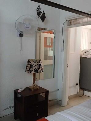 A room with a bed, a bedside table with a lamp, a wall-mounted fan, and a mirror. - Executive Studio in Kisumu. Complimentary wifi, secure parking & quiet stay (Kisumu)