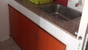 Een keuken met een RVS spoelbak, een groene zeef en een koffiekop op het aanrecht.