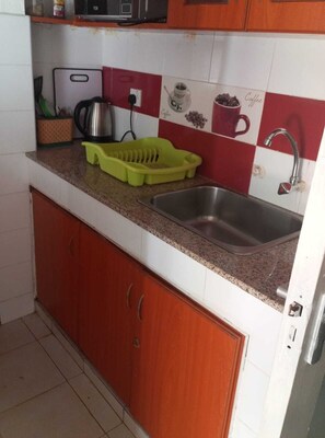 A kitchen with a stainless steel sink, a green colander, and a coffee cup on the counter. - Executive Studio in Kisumu. Complimentary wifi, secure parking & quiet stay (Kisumu)