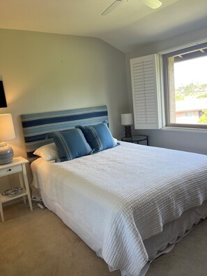 A bedroom with a bed, bedside tables, a lamp, a window with blinds, and a ceiling fan.