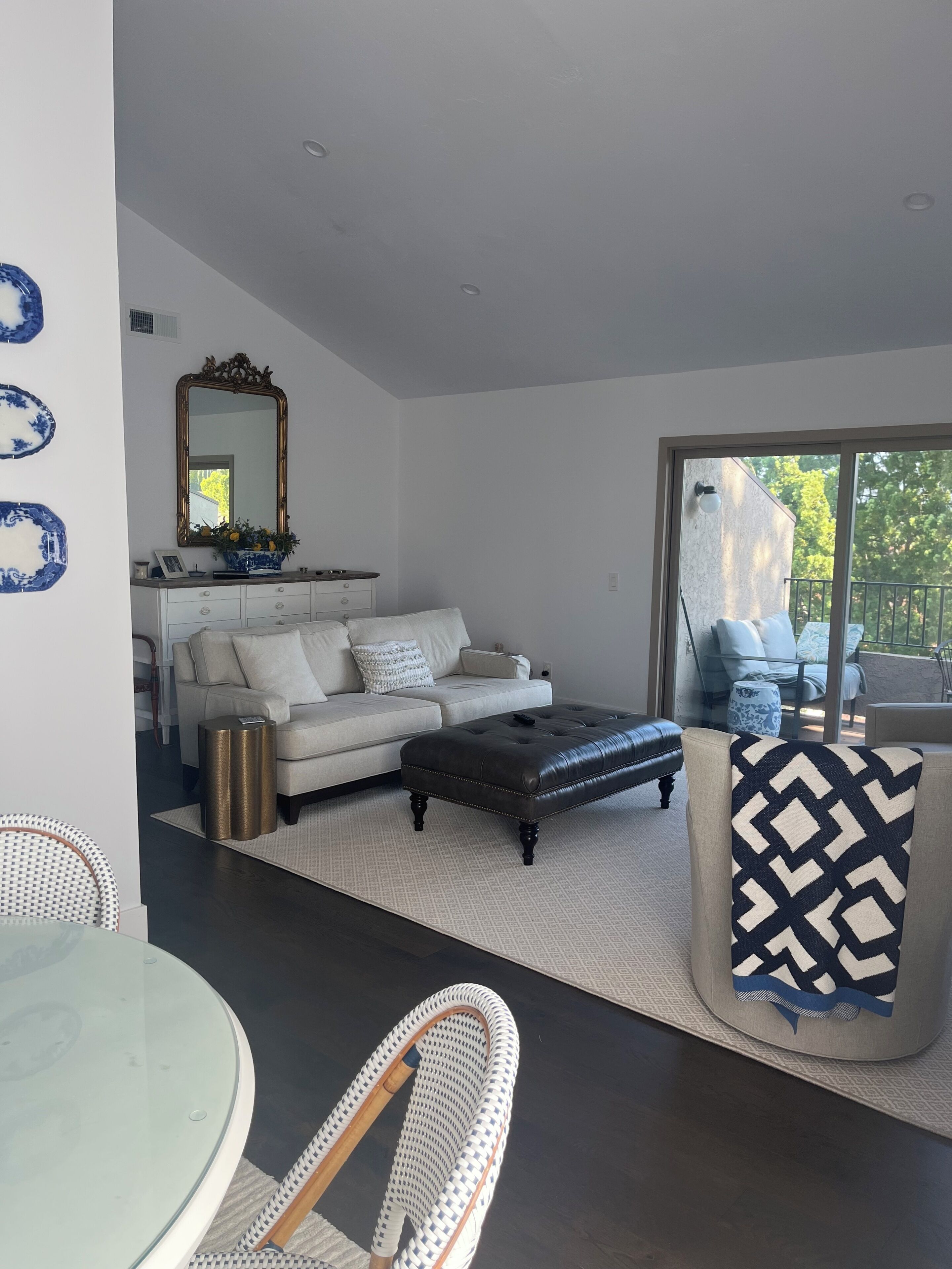 A modern living room with a sofa, ottoman, and a dining area with a glass table and chairs.
