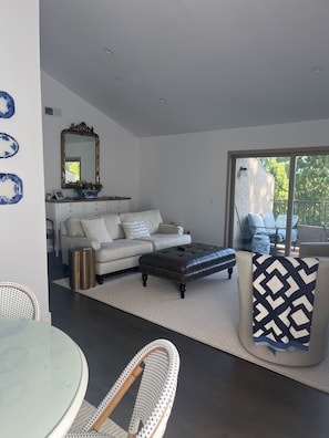 A modern living room with a sofa, ottoman, and a dining area with a glass table and chairs.