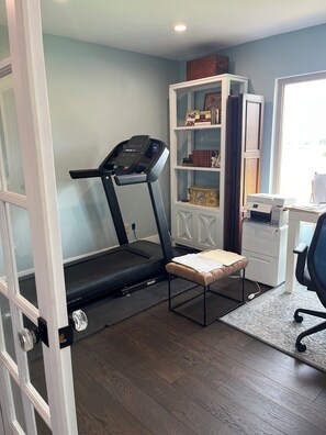 A home office with a treadmill, a desk, and a bookshelf.