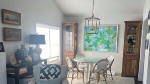 Ein Wohnzimmer mit einem grauen Sessel, einem Esstisch mit Stühlen, einer Kandelaber und einem großen Gemälde an der Wand.