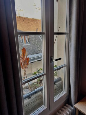 A window with a view of a building's exterior, a radiator, and a plant inside. -     Parisian Elegance & Modern Comfort on Île Saint-Louis (Paris)