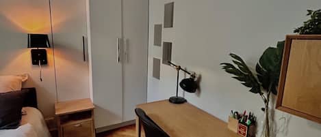 Une chambre avec un lit, un bureau, une armoire, une lampe et une plante.