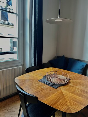 A dining area with a round wooden table, black chairs, a woven basket, a hanging light fixture, and a view through a window. -     Parisian Elegance & Modern Comfort on Île Saint-Louis (Paris)