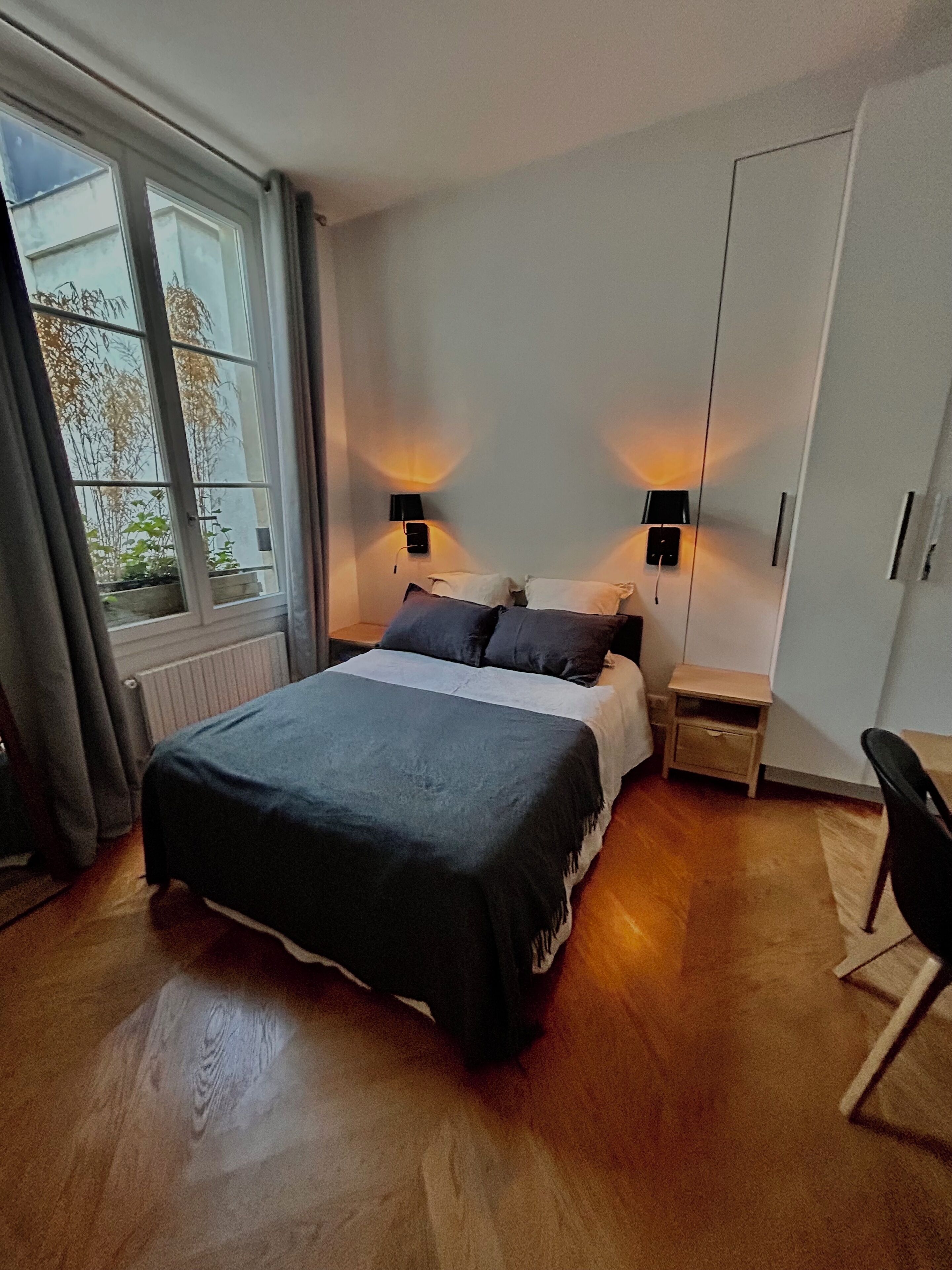 Una camera da letto con un letto, lampade da comodino, un comodino, un armadio e una finestra con tende.