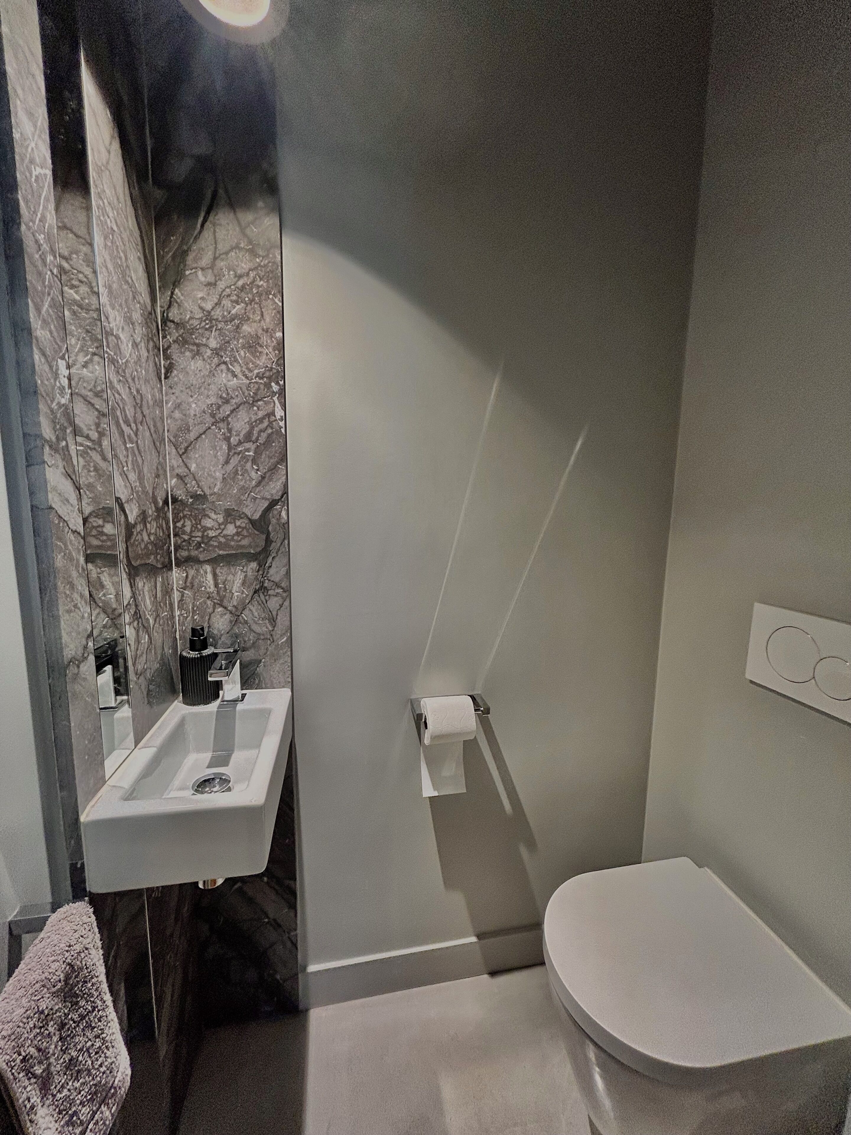 A bathroom with a marble wall, a white sink, and a toilet.