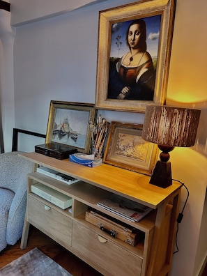 Una stanza con una scrivania in legno, una lampada, un quadro raffigurante una donna e una libreria.