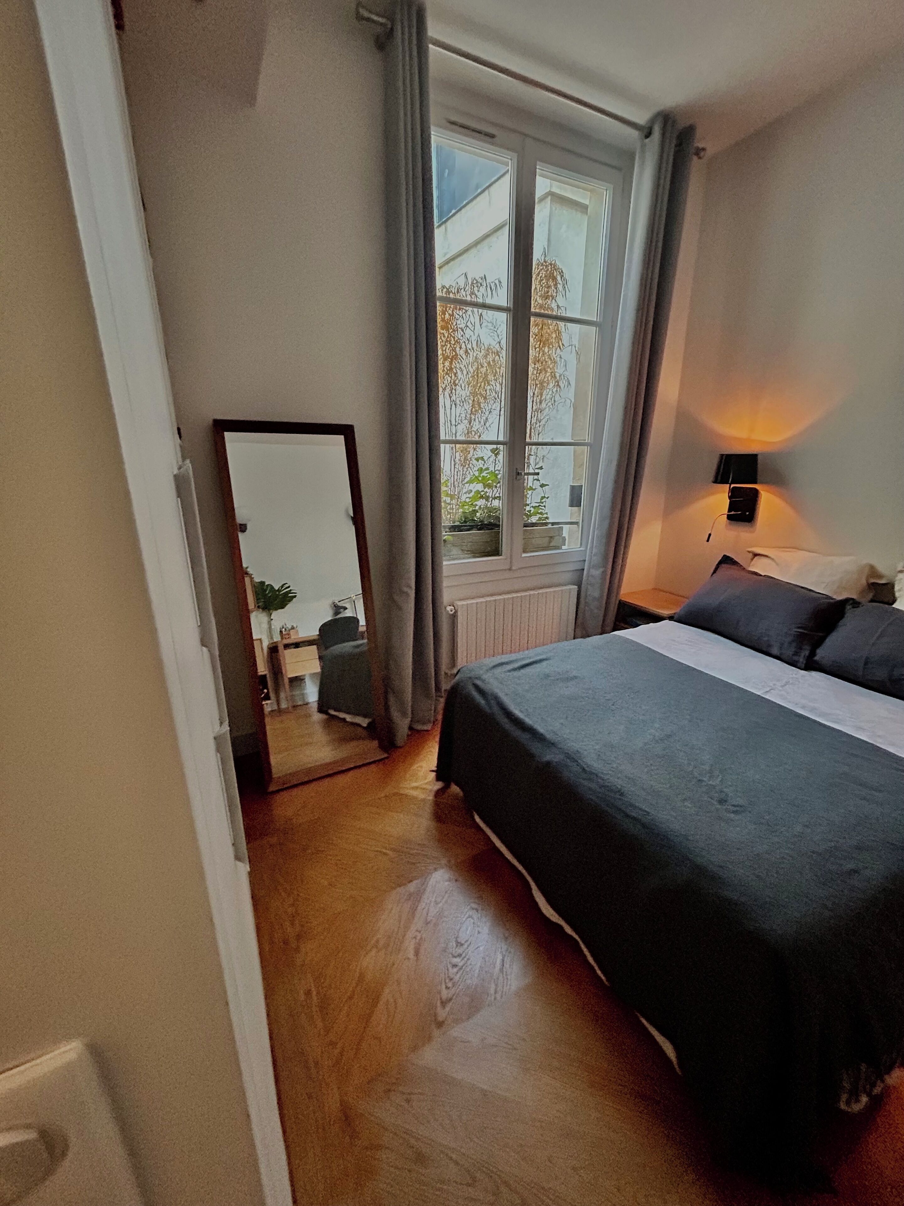 Ein Schlafzimmer mit einem großen Bett, einem Fenster mit Vorhängen, einer Nachttischlampe und einer Heizung.