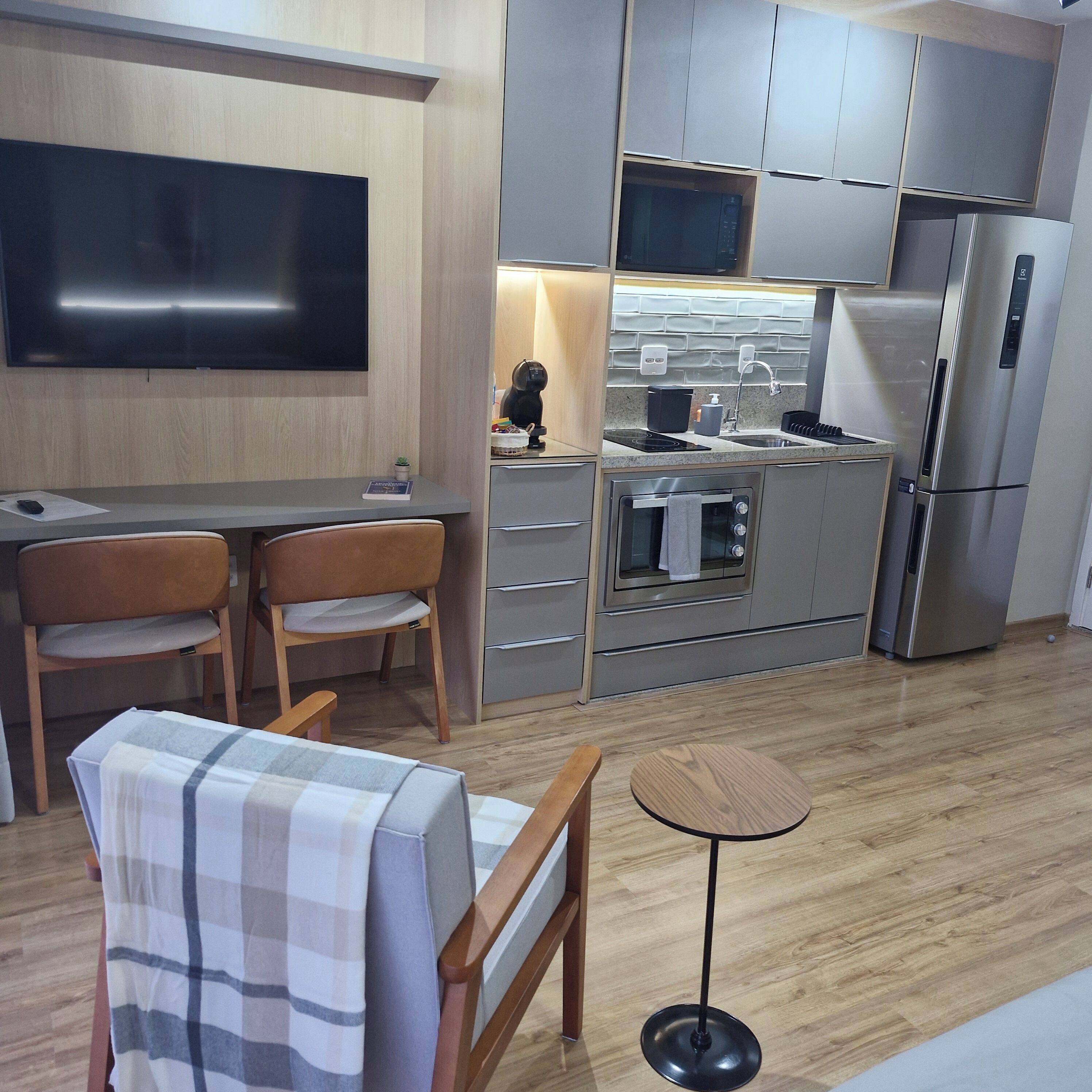 Une cuisine moderne équipée d’un téléviseur à écran plat, d’un coin repas avec deux chaises, une petite table et un canapé recouvert d’un tissu à carreaux.