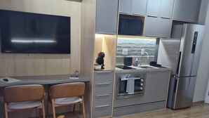 Eine moderne Küche mit Fernseher, einer Essecke mit zwei Stühlen, einem kleinen Tisch und einer Couch mit kariertem Bezug.