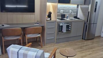 Cozinha moderna com televisão de tela plana, área de jantar com duas cadeiras, uma mesa pequena e um sofá com capa xadrez.