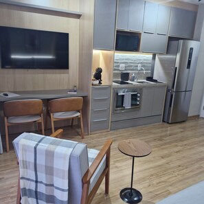 Een moderne keuken met een flatscreen televisie, een zithoek met twee stoelen, een klein tafeltje en een bank met een geruit hoesje.