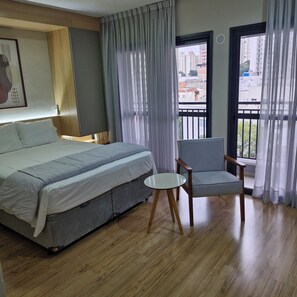 A hotel room with a bed, a chair, a small table, and a window with curtains. - Fully equipped studio apartment with queen bed, 140m from Alto do Ipiranga metro station, with air conditioning. (São Paulo)