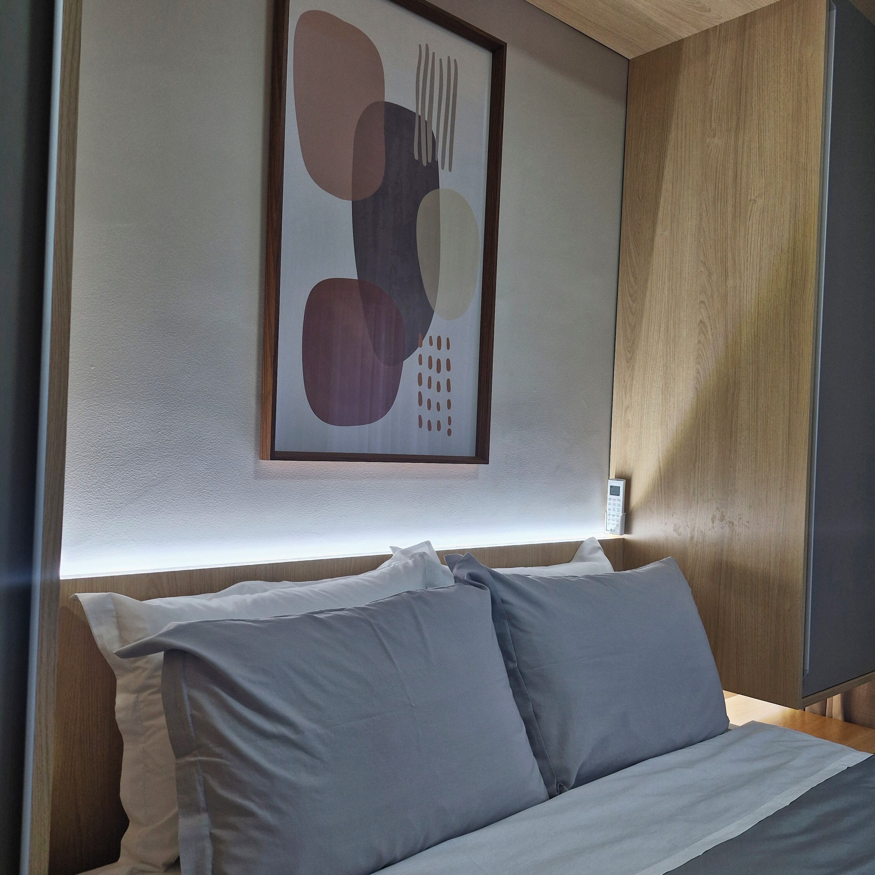 A bed with grey bedding, a wall-mounted artwork, and a wooden panel.
