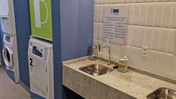 Casa de banho pública com dispensador de ar quente, lavatório, espelho e um sinal com instruções de cuidados.