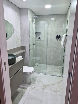 Een moderne badkamer met een douche met glazen wand, een toilet en een wastafel met een waskom.
