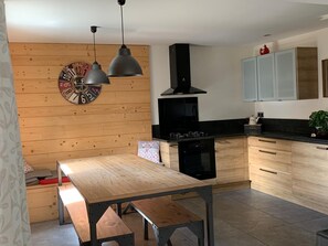 A modern kitchen with wooden cabinetry, a black stove, and pendant lighting. - Vrbo Property (Molines-en-Queyras)