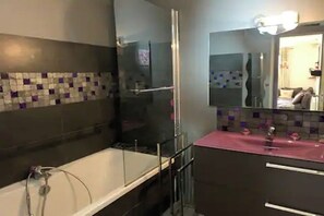 A modern bathroom with a glass shower enclosure, a white bathtub, and a vanity with a pink countertop. - Vrbo Property (Molines-en-Queyras)