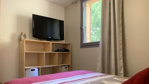 Ein Schlafzimmer mit einem Bett, einem Fernseher auf einem Holzregal und einem Fenster mit Vorhängen.