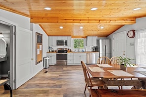 A modern kitchen with white cabinets, stainless steel appliances, and a wooden ceiling.
