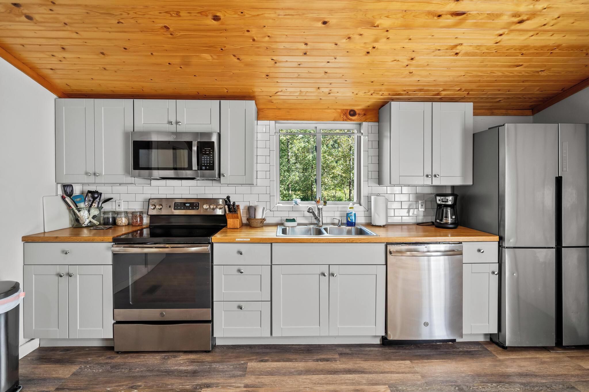 A modern kitchen with grey cabinets, stainless steel appliances, and a wooden ceiling.