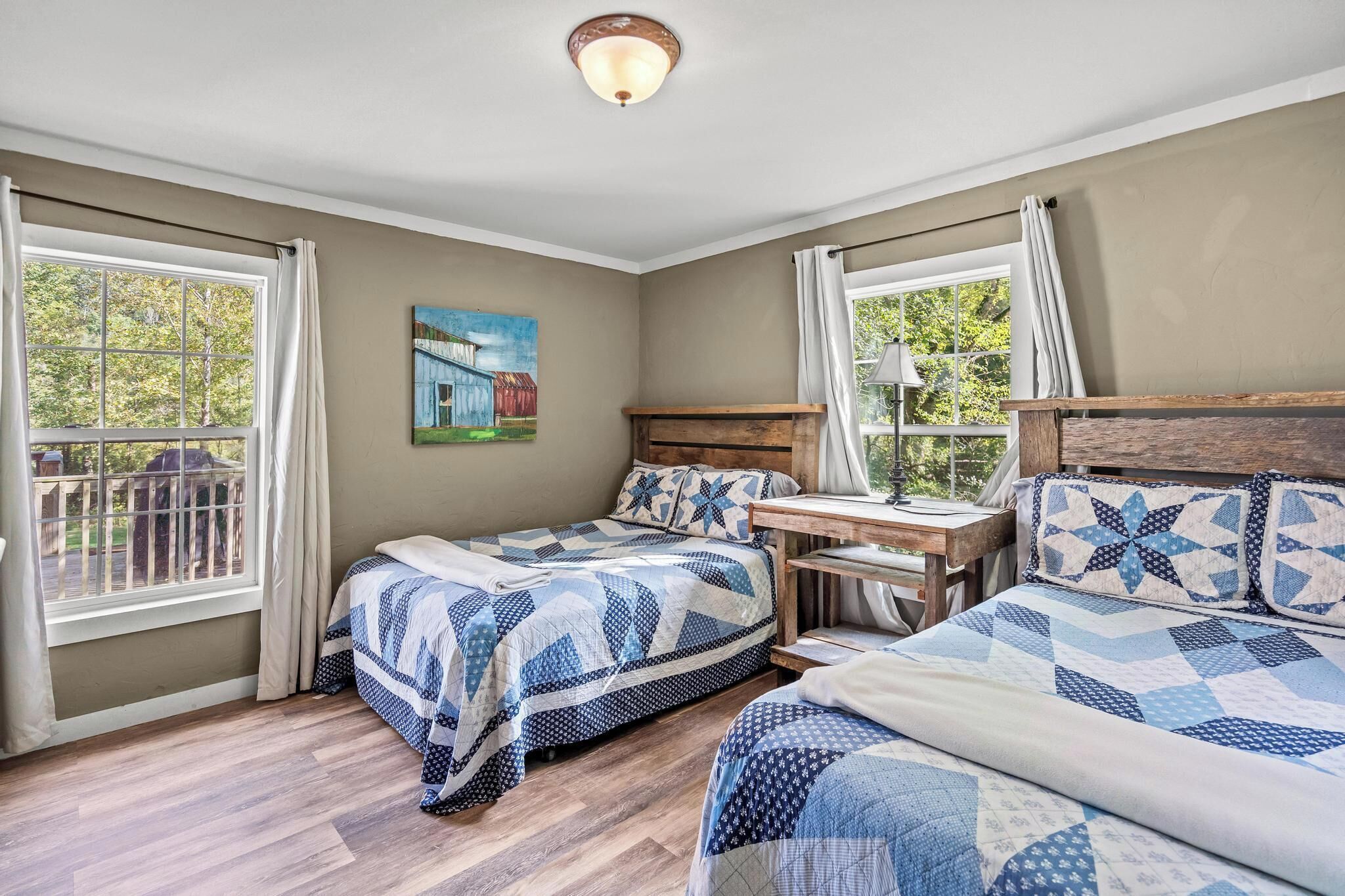 A bedroom with two beds, a wooden headboard, a nightstand, a lamp, and a painting on the wall.