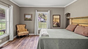 A bedroom with a bed, a chair, a window, and a painting. - South Fork River Farmhouse with River Access (Stanton)