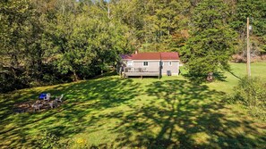 A house with a deck, surrounded by trees and a grassy yard.