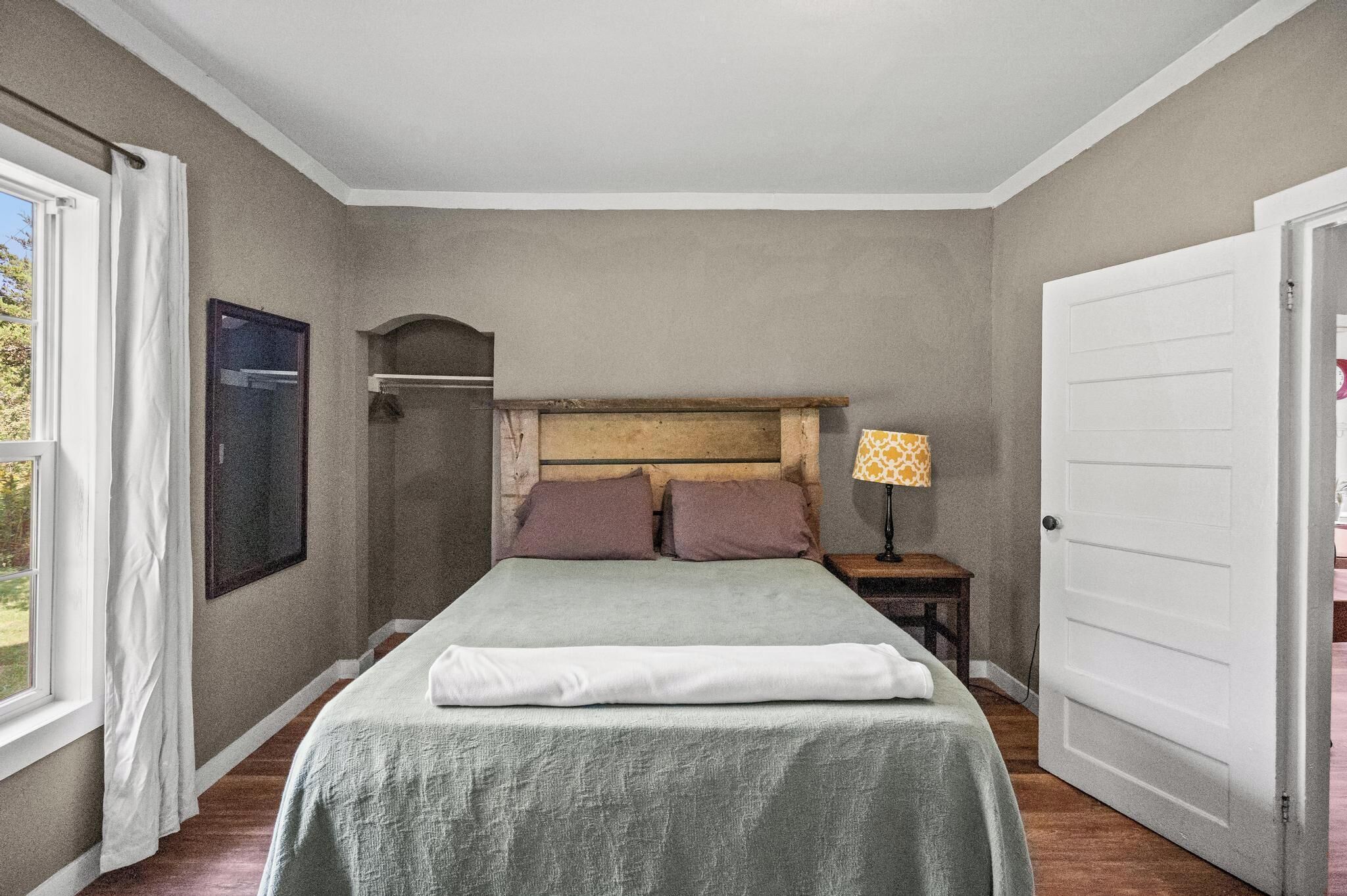 A bedroom with a bed, a nightstand, a lamp, a door, and a window.