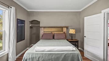 Une chambre à coucher avec un lit, une table de chevet, une lampe, une porte et une fenêtre.