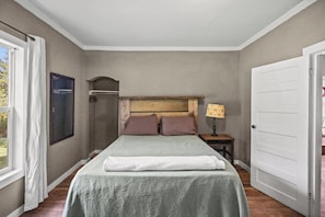A bedroom with a bed, a nightstand, a lamp, a door, and a window.